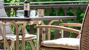 Una mesa con una botella de vino, una copa y una taza decorativa en un balcón con sillas de mimbre.