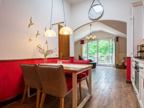 A dining area with a red cushioned bench, a wooden table, and two chairs. A large wall clock and decorative wall art are visible. - L-43 - Residence Laguna Whg L-43 .. (Kühlungsborn)