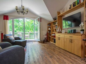 A cozy living room with a large window, a wooden bookshelf, and a flat-screen TV. - L-43 - Residence Laguna Whg L-43 .. (Kühlungsborn)