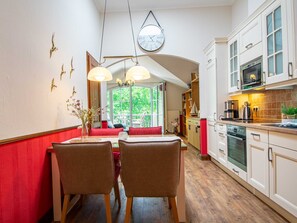 A kitchen with white cabinets, a microwave, and a stove. There is a dining area with two chairs and a table, and a clock on the wall. - L-43 - Residence Laguna Whg L-43 .. (Kühlungsborn)