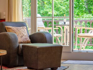 Una sala de estar con sofá, reposapiés, una mesita y vistas a un balcón con mobiliario exterior.