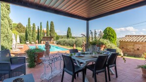 Eine überdachte Terrasse mit Pool, Gartenmöbeln und Blick auf die umliegende Landschaft.