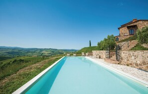 Une piscine bordée d’un mur de pierre d’un côté, avec en arrière-plan une vue sur des collines ondoyantes.