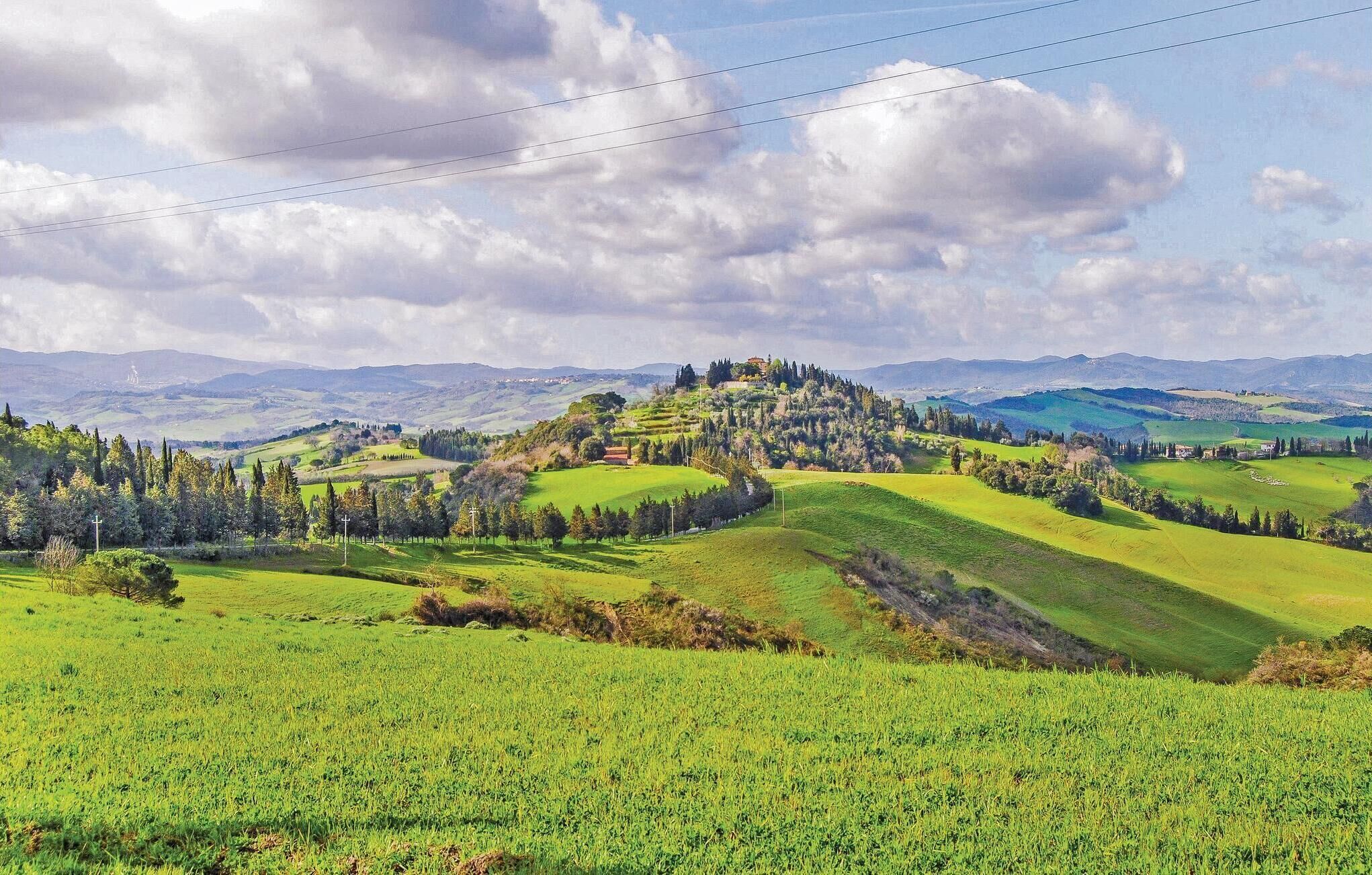 Ein weitreichender Blick auf eine üppige, grüne Landschaft mit sanften Hügeln, einem markanten Haus auf einem Hügel und entfernten Bergen.