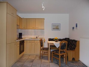 A compact kitchen with wooden cabinets, a built-in oven, and a small dining area with a table and two chairs. - Apartment No. 3 - To the little mermaid (Friedrichskoog)