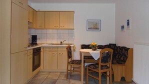 Une cuisine compacte avec des meubles en bois, un four encastré et un petit coin repas comprenant une table et deux chaises.