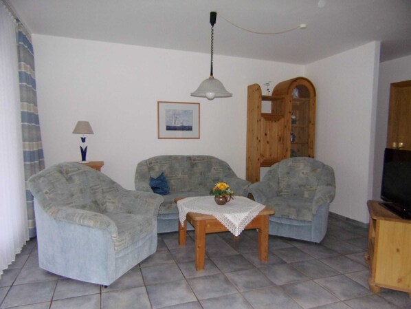 A living room with two armchairs, a small table with a vase, a lamp, a framed picture, and a wooden cabinet. - Apartment No. 3 - To the little mermaid (Friedrichskoog)