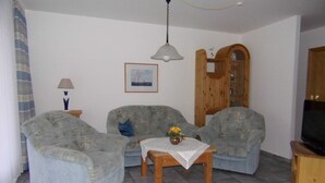 Un salon avec deux fauteuils, une petite table sur laquelle est posé un vase, une lampe, un tableau encadré et un meuble en bois.