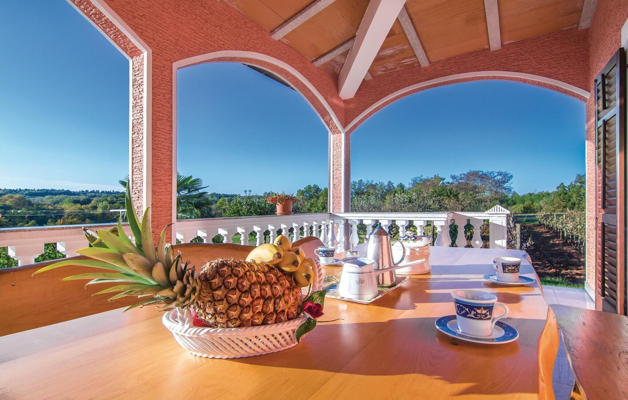 Una terraza con una mesa dispuesta para el té, una cesta de frutas y vistas al campo.