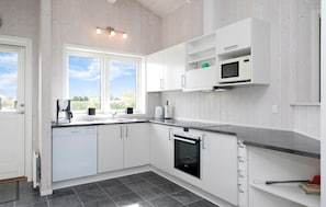 A modern kitchen with white cabinetry, a built-in oven, and a microwave. There is a window providing natural light and a view of the outdoors. - Lovely home in Hadsund with sauna (Hadsund)