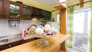Una cocina con armarios de madera, un refrigerador con puerta de vidrio y una ventana con vista a la vegetación.