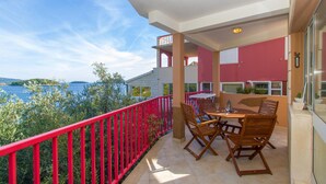 Un balcón con barandilla roja, muebles de madera y vista al mar.