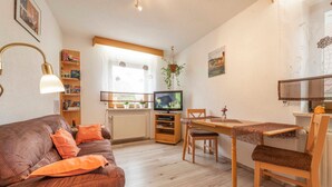 A cozy living room with a brown leather sofa, orange cushions, a wooden dining table, and a television. - Dormitory Room - Small Room (Heiligenstadt i.OFr.)