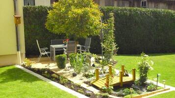 Een verzorgde tuin met een houten terras, stoelen en een tafel.
