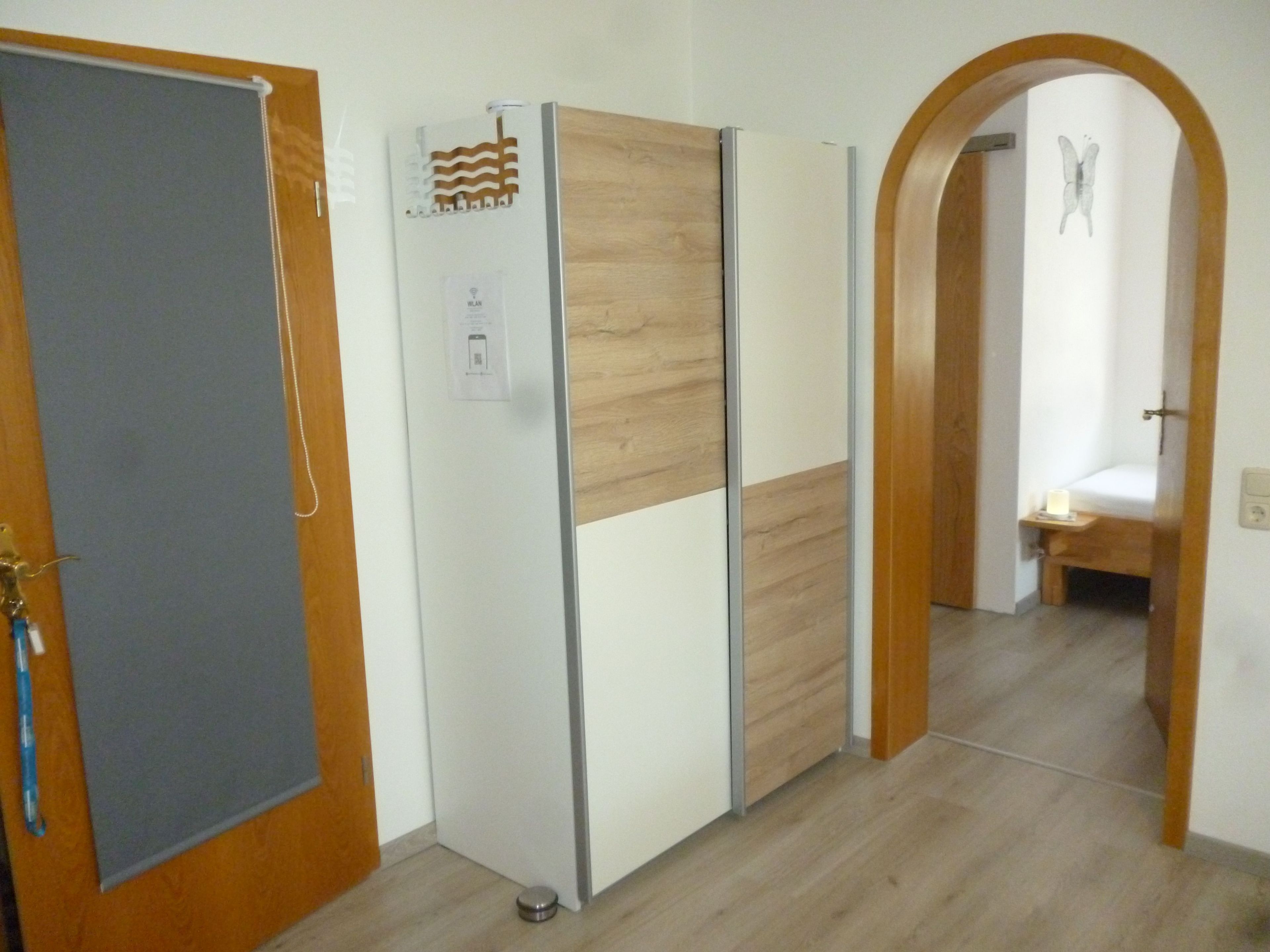 Ein Zimmer mit Holztür, einem Schrank mit Spiegel und einem Bett im angrenzenden Raum.