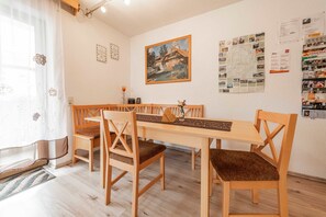 A dining area with a wooden table and chairs, a painting on the wall, and a bulletin board with various papers. - Dormitory Room - Small Room (Heiligenstadt i.OFr.)