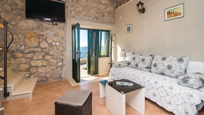 Una habitación acogedora con pared de piedra, un televisor sobre una puerta, un sofá con cojines estampados y una mesita con un objeto decorativo.