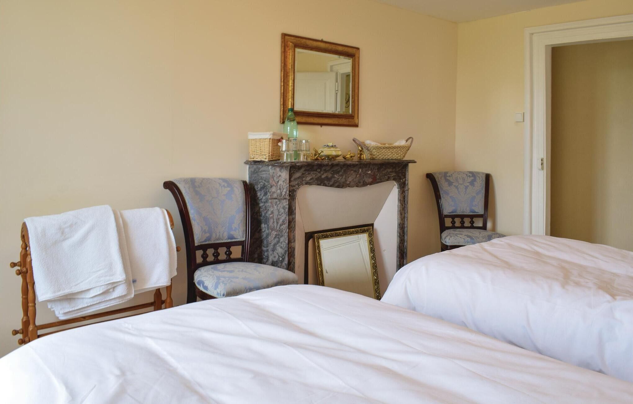 A hotel room with two beds, a fireplace, a mirror, and two armchairs.