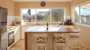 A kitchen with a wooden island, white chairs, a microwave, a coffee maker, and a clock on the wall. - Amazing home in Rochefort (Rochefort)