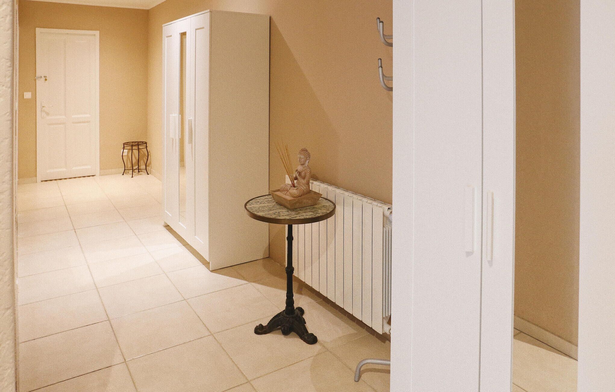 A hallway with a tiled floor, a white door, a small table with a Buddha statue, and a radiator.