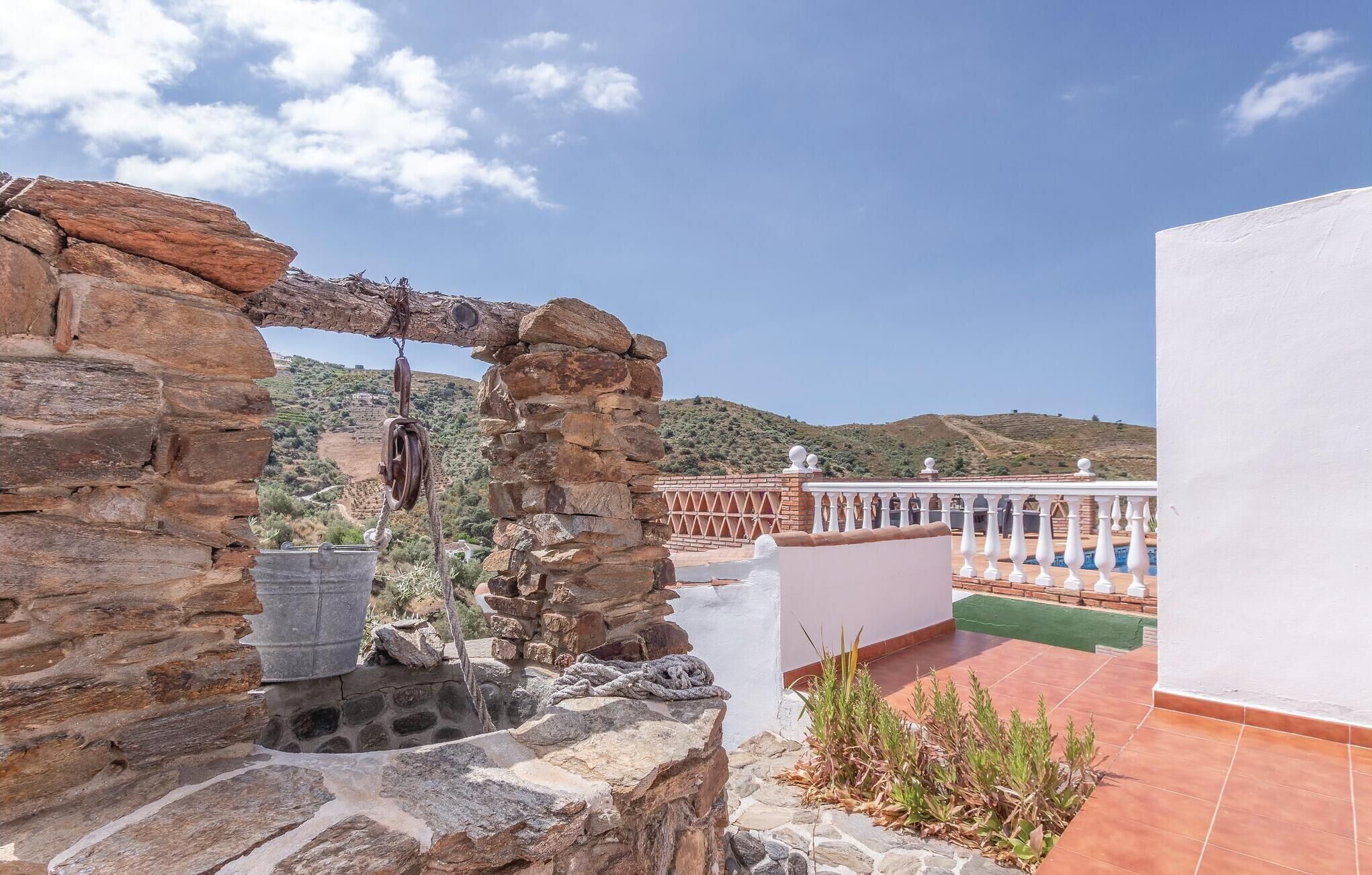 A stone archway leading to a terrace with a pool and a view of hills.