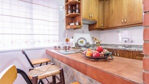 A kitchen with a central island, wooden cabinets, and a window with a floral curtain. - Amazing home in Torrox Costa with WiFi (Torrox Costa)