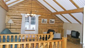 Ein gemütliches Blockhaus-Interieur mit einer Holztreppe, einem Fernseher und einem Fenster mit Vorhängen.