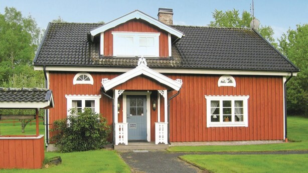 Ein rotes Holzhaus mit grauem Dach, einer Veranda und einem kleinen Garten.