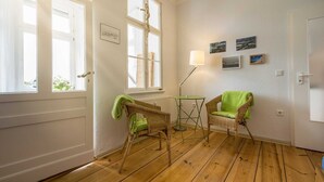 Een kamer met houten vloer, rieten stoelen met groene kussens, een kleine tafel en een lamp.