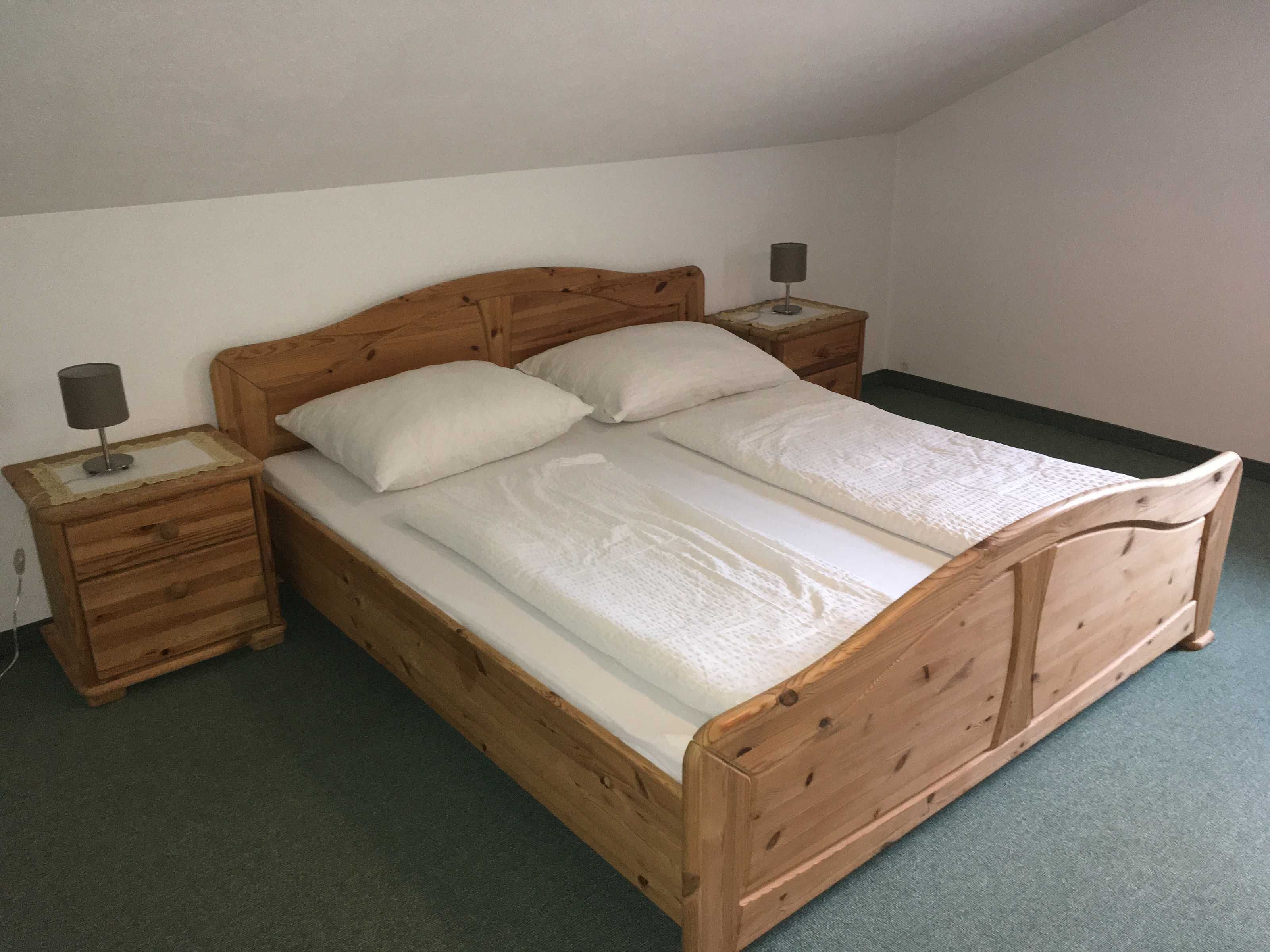 Una cama de madera con dos almohadas y una mesita de noche con una lámpara.