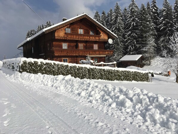 Eine Holzchalet mit Balkon, umgeben von schneebedeckten Bäumen und einem mit Schnee bedeckten Heckenbewuchs.