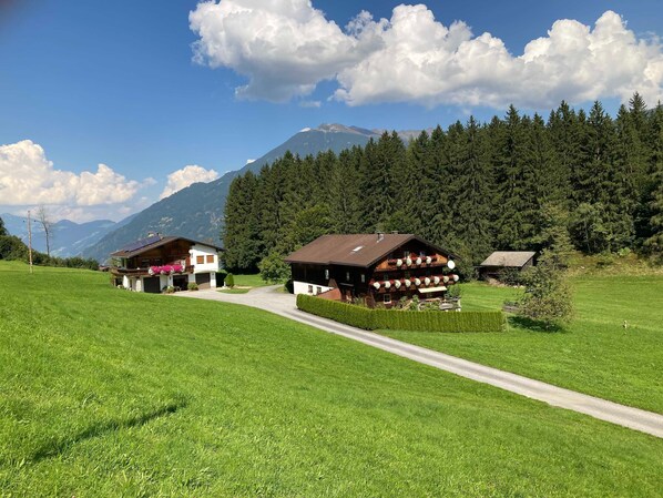 A rural mountain setting with two wooden buildings, a clear sky, and a mountain in the background.