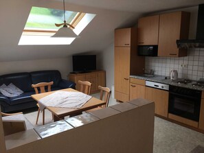 A compact kitchen with wooden cabinets, a dining area, and a TV on a cabinet.