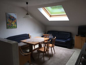A compact living space with a dining area, a sofa, a television, and a skylight.