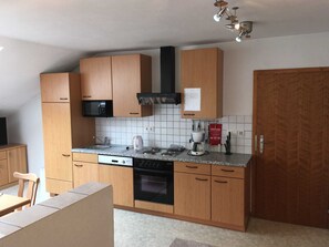 A compact kitchen with wooden cabinets, a microwave, a stove, and a coffee maker.