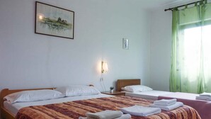 A hotel room with two beds, a painting on the wall, a bedside lamp, and a window with green curtains.
