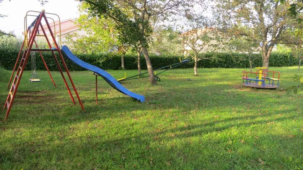 Een speeltuin met een glijbaan en schommels in een grasveld met bomen.