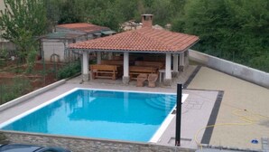 A swimming pool with a tiled deck, a covered seating area with benches, and a hose for pool maintenance.