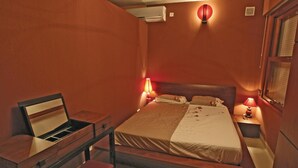 Une chambre d’hôtel comprenant un lit, des tables de chevet, un bureau avec une chaise et un climatiseur fixé au mur.
