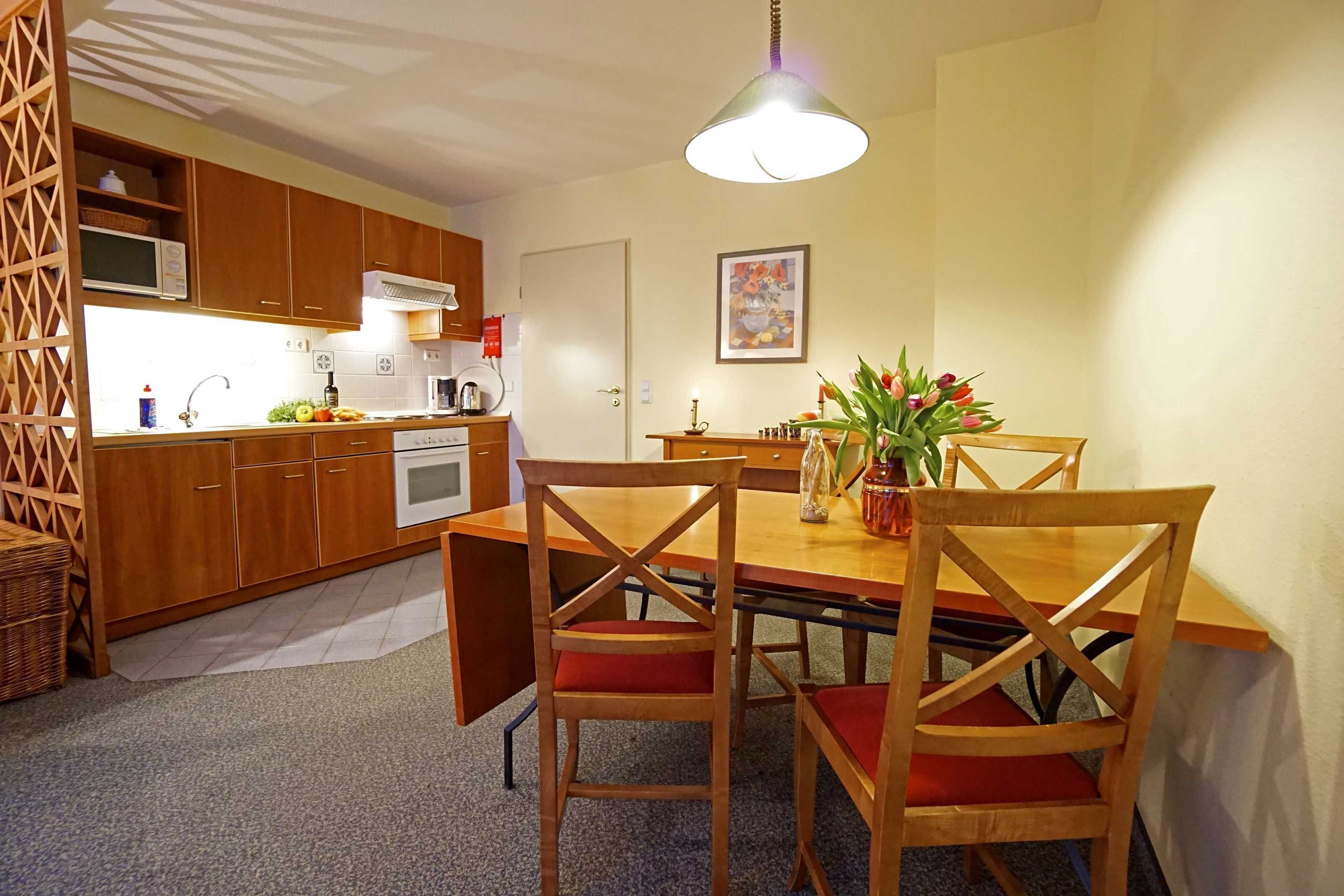 A compact kitchen with wooden cabinets, a microwave, and a dining area with a table and chairs.