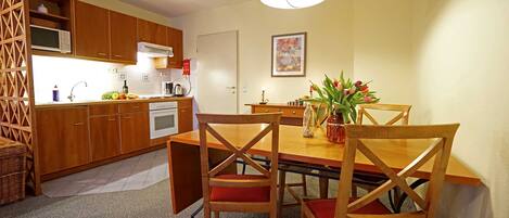 A compact kitchen with wooden cabinets, a microwave, and a dining area with a table and chairs.