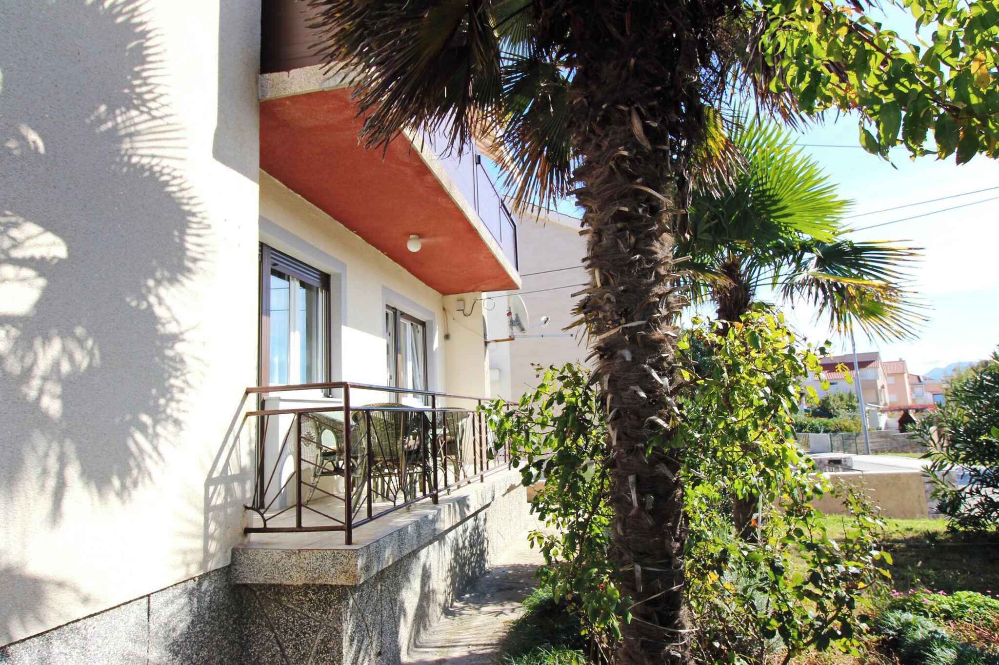 A building with a balcony, palm trees, and a clear sky.