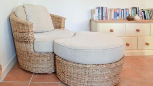 A wicker armchair with a cushion and ottoman in a room with tiled flooring and a bookcase.