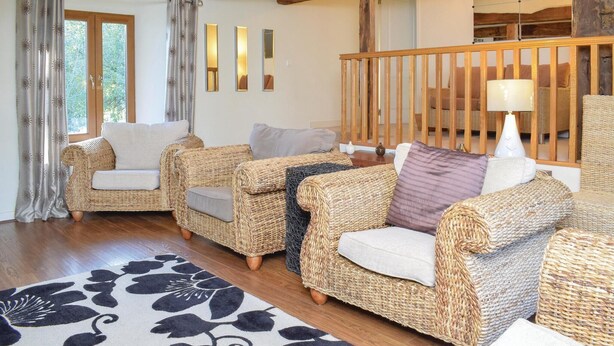 A cozy living room with wicker furniture, a patterned rug, and a wooden railing.