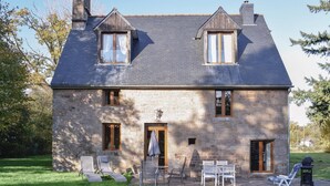 A stone house with two dormer windows, a chimney, and a small porch with outdoor seating.