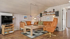 Una sala de estar con un mueble de televisión de madera, un sillón de cuero, una mesa de centro de madera y una alfombra estampada.