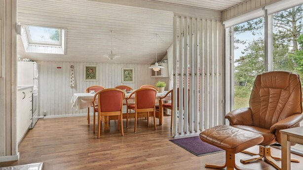 Comedor con mesa dispuesta para cuatro personas, sillas de madera y un ventanal con vistas a árboles.
