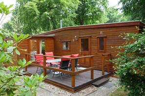 A wooden cabin with a deck, outdoor seating, and a chimney.