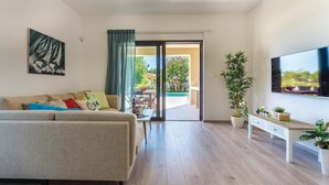 A living room with a sofa, a TV, a dining table, and a view of the outside. - Beach front home in Premantura (Premantura)