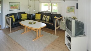 A living room with a black leather sofa, a wooden coffee table, a television on a white stand, and a window with a view of greenery.
